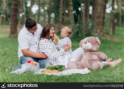 Mom, dad and little daughter on the picnic with teddy bear in the park outdoors. The concept of summer holiday. Mother&rsquo;s, father&rsquo;s, baby&rsquo;s day. Family spending time together on nature. Family look.. Mom, dad and little daughter on the picnic with teddy bear in the park outdoors. The concept of summer holiday. Mother&rsquo;s, father&rsquo;s, baby&rsquo;s day. Family spending time together on nature. Family look