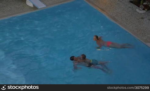 Mom, dad and son bathing in the pool. Father swimming on the back and child holding him