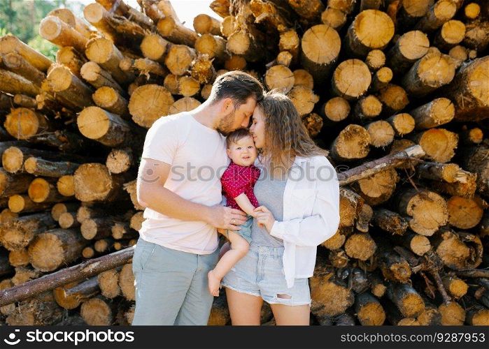 Mom, dad and their baby son are kissing in a pile of tree trunks.