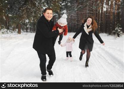 mom, dad, daughter and little son having fun in the winter forest. Active parents with children run in the snowy forest.. mom, dad, daughter and little son having fun in the winter forest. Active parents with children run in the snowy forest