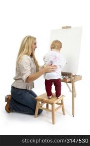 Mom helping baby girl to paint at large wooden easel.