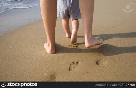 mom helps to make the child&rsquo;s first steps on the beach