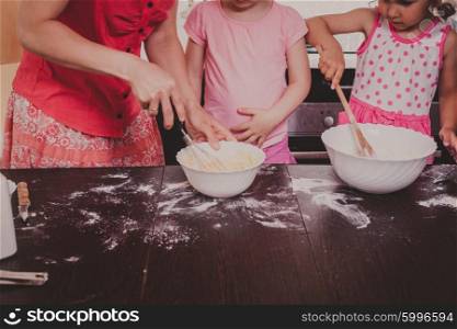 Mom is baking cookies with her kids at home kitchen. Cooking together