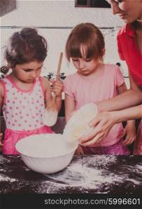 Mom is baking cookies with her kids at home kitchen. Cooking together