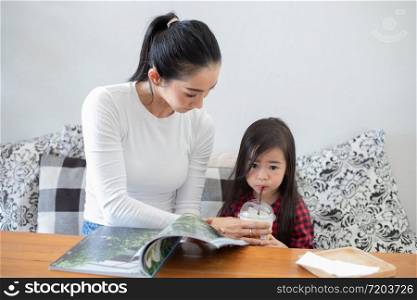 Mom is raising a glass of cold milk, daughter drinking and teaching her daughter to read a book.