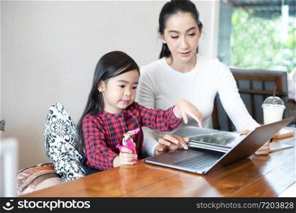 Mom is teaching her daughter to read a book and playing notebook.