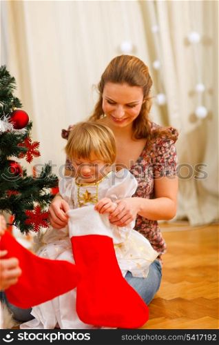 Mom looking with daughter inside of Christmas socks near Christmas tree