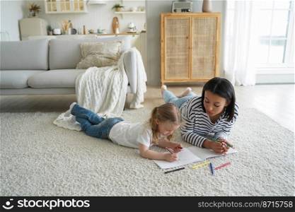 Mom or babysitter and little preschooler kid girl painting together lying on floor carpet in living room. Mother and daughter drawing. Child creativity development, children’s education concept.. Mom or babysitter and little preschooler kid girl daughter painting together lying on floor carpet