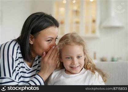 Mom or babysitter whisper secret to cute little elementary kid daughter. Mother whispering in girl’s ear, telling gossip story to child. Family unity, trustful relationship, child care concept.. Mom or babysitter whisper secret to little elementary kid girl daughter. Family unity, child care