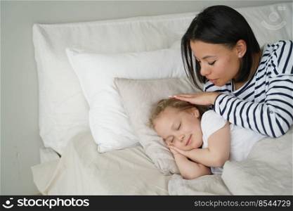 Mom puts daughter to bed, stroke head of small child during daytime nap. Calm kid girl rest sleeping lying on soft pillow under fresh duvet. Healthy sleep in children, childcare.. Mother puts daughter to bed, lying on soft pillow. Daytime nap, healthy sleep in children, childcare