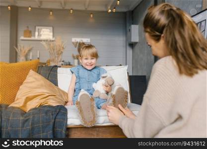 Mom puts on her daughter’s slippers while sitting on the couch in the house