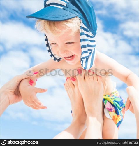 Mom throws up her smiling baby boy in the blue sky,summer time.