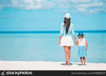 Mom with little daughter on the beach. Back view of family walking on the seashore. Beautiful mother and daughter at Caribbean beach enjoying summer vacation.