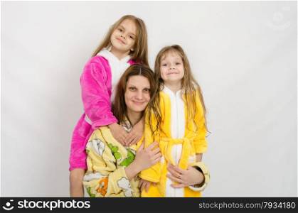 Mom with two daughters sitting in the bath robes on a white background. Portrait of a mother and two daughters in bath robes