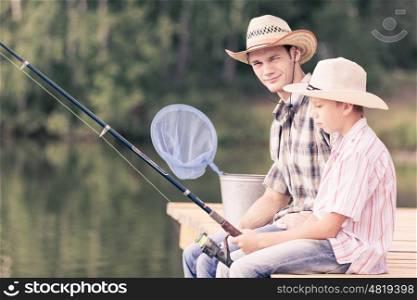 Moments of family togetherness. Father and son sitting on bridge and fishing
