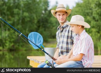 Moments of family togetherness. Father and son sitting on bridge and fishing