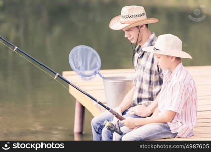 Moments of family togetherness. Father and son sitting on bridge and fishing