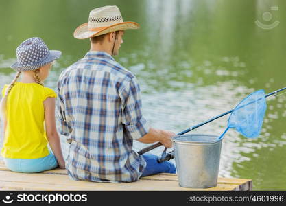 Moments of family togetherness. Rear view of father and daughter sitting on bridge and fishing