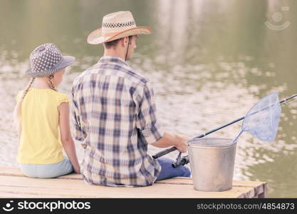 Moments of family togetherness. Rear view of father and daughter sitting on bridge and fishing