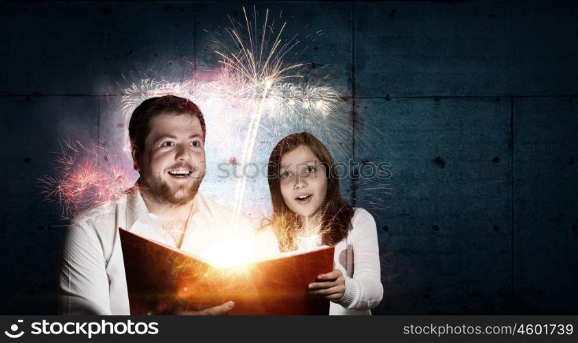 Moments of family togetherness. Young father and daughter read book and light coming out of pages