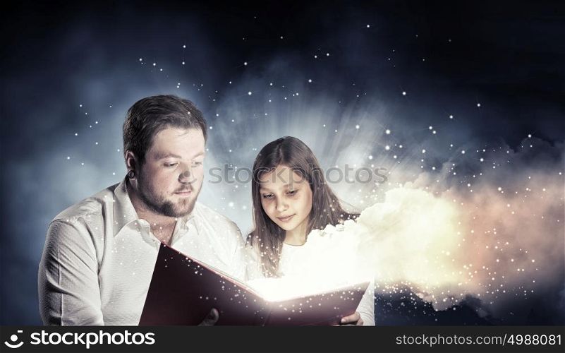 Moments of family togetherness. Young father and daughter read book and light coming out of pages