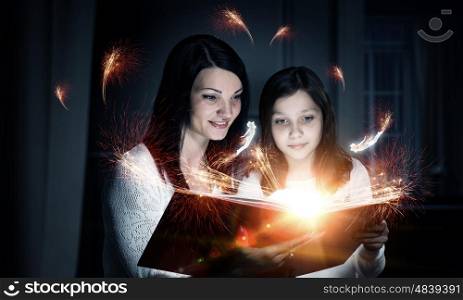 Moments of family togetherness. Young mother and daughter read book and light coming out of pages