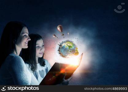 Moments of family togetherness. Young mother and daughter read book and light coming out of pages. Elements of this image are furnished by NASA