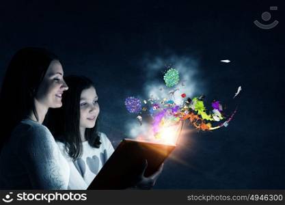 Moments of family togetherness. Young mother and daughter read book and light coming out of pages