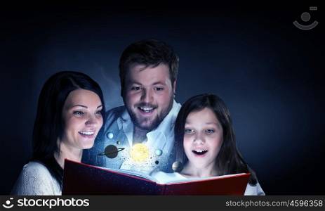 Moments of family togetherness. Young mother father and daughter read book and light coming out of pages