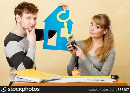 Money and real estate problems. Young worried couple with paper model of house and key. Young marriage calculate expenses.. Young couple worried about money for house.