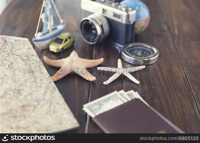 money banknote, compass, passport, globe, camera, map, car ship and starfish figurine on wooden table for use as traveling concept (vintage tone and selected focus)