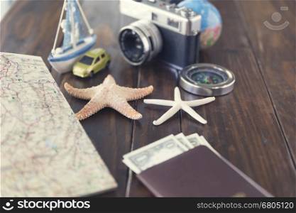 money banknote, compass, passport, globe, camera, map, car ship and starfish figurine on wooden table for use as traveling concept (vintage tone and selected focus)
