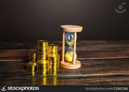 Money coins and an sand hourglass. Fair hourly wages. Time is money. Deposit. Profitability and return on investment. Balance between life and career. Retirement savings, long-term investments.