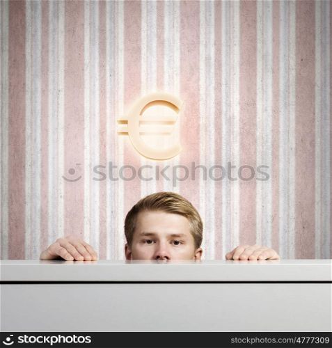 Money concept. Half of face of young man looking out from under table