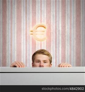 Money concept. Half of face of young man looking out from under table