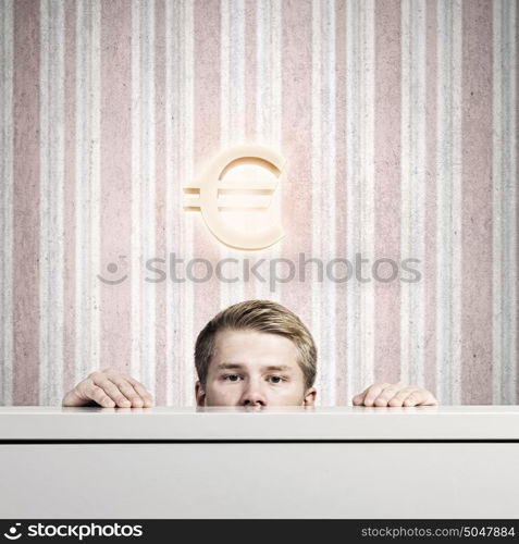 Money concept. Half of face of young man looking out from under table