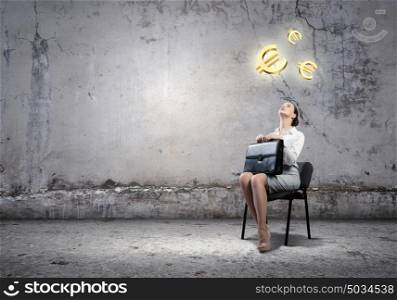 Money exchange. Image of businesswoman sitting on chair with suitcase in hands looking at euro symbols above