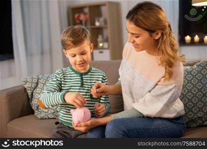 money, family and people concept - happy smiling mother and thrifty little son putting euro coin to piggy bank at home. mother and little son with piggy bank at home