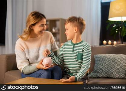 money, family and people concept - happy smiling mother and thrifty little son putting euro coin to piggy bank at home. mother and little son with piggy bank at home