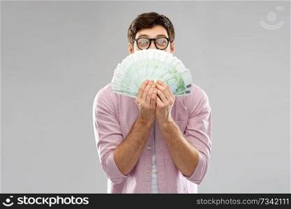 money, finance, business and people concept - happy young man in glasses with fan of one hundred euro bank notes over grey background. happy young man in glasses with fan of euro money