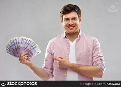 money, finance, business and people concept - smiling young man showing fan of five hundred euro bank notes over grey background. smiling young man showing fan of euro money