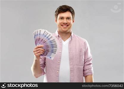 money, finance, business and people concept - smiling young man with fan of five hundred euro bank notes over grey background. smiling young man with fan of euro money over grey