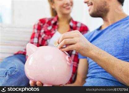 money, finance, investment, saving and people concept - close up of happy couple putting euro coin to piggybank