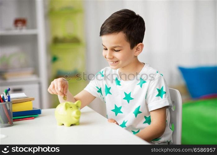 money, finances, childhood and people concept - smiling little boy putting coin into piggy bank at home. little boy putting coin into piggy bank at home
