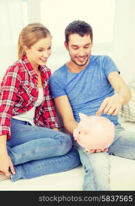 money, home, finance and relationships concept - smiling couple with piggybank sitting on sofa