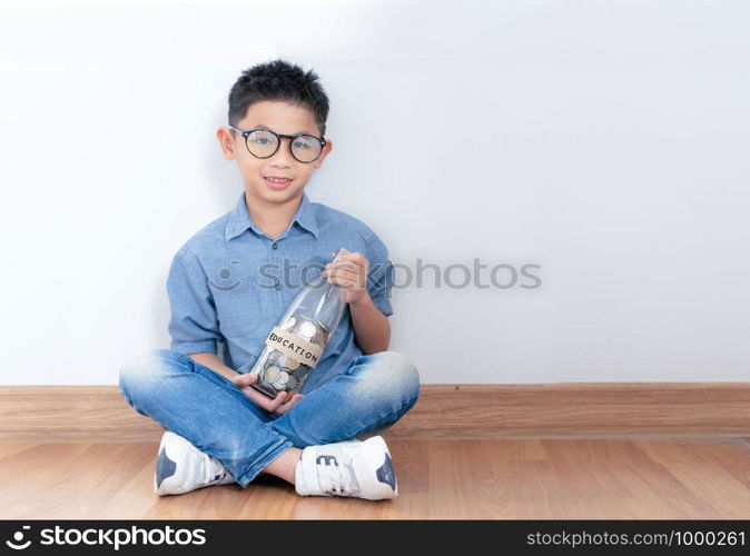 money in asian kid's hands.happy asian boy holding glass bottle and saving money into glass bottle.Education and saving concept.