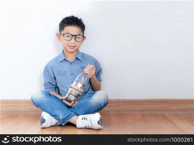 money in asian kid's hands.happy asian boy holding glass bottle and saving money into glass bottle.Education and saving concept.