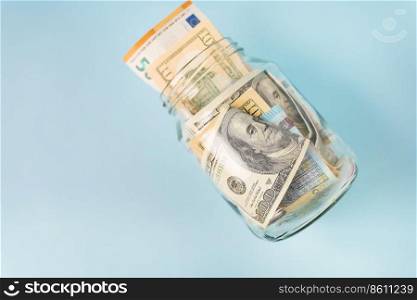 Money in international currency, including euro, dollar lies in a glass jar on a blue background. Place for an inscription. Money in international currency, including euro, dollar lies in a glass jar on a blue background. Place for an inscription.