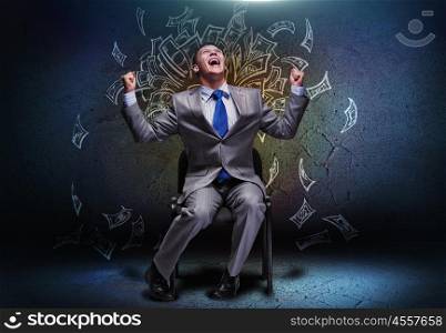 Money making. Joyful businessman sitting on chair under money rain