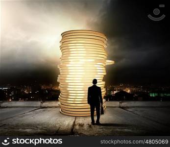 Money making. Rear view of businessman with suitcase looking at stack of coins